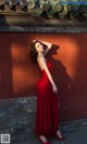 A woman in a red dress leaning against a wall.