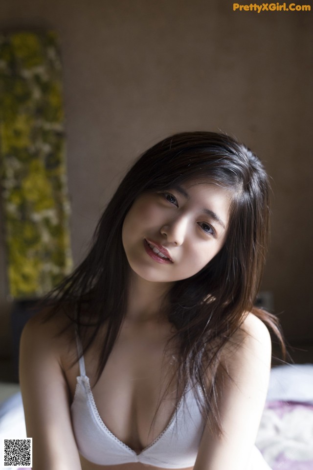 A woman in a white bra sitting on a bed.