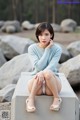 A woman sitting on a concrete bench in a blue sweater.