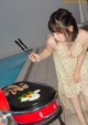 A woman in a yellow dress is cooking food on a grill.