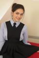 A young woman in a school uniform sitting on a bed.