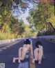 Two naked women sitting on the side of a road.