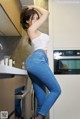 A woman in a white top and blue jeans standing in a kitchen.