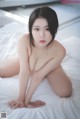 A naked asian woman sitting on a bed.