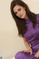 A woman in a purple dress sitting on a bed.
