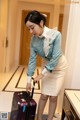 A woman in a blue shirt and white skirt with a suitcase.