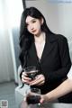 A woman in a black suit holding a glass of wine.