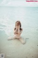 A woman sitting in the water with her hands covering her face.