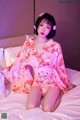 A woman in a pink kimono sitting on a bed.