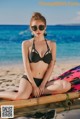 A woman in a black bikini sitting on a beach.