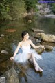 A woman in a white dress sitting on a rock in the water.