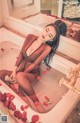 A woman sitting in a bathtub with rose petals on the floor.