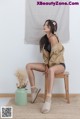 A woman sitting on a wooden stool next to a vase of flowers.