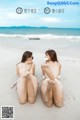 A couple of women sitting on top of a sandy beach.