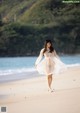 A woman in a white dress walking on a beach.