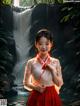 A woman in a red dress standing in front of a waterfall.