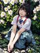 A girl sitting on the ground in front of a bush of flowers.