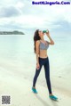 A woman standing on a beach drinking from a bottle.