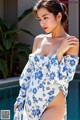 A woman in a blue and white floral dress posing by a pool.