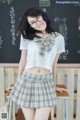 A woman wearing glasses and a plaid skirt posing in front of a blackboard.