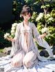 A woman in a white kimono sitting on a rock with flowers.