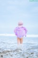 A little girl with pink hair standing in the ocean.