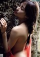 A woman in a red dress leaning against a rock.