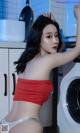 A woman in a red top and white panties standing in front of a washing machine.